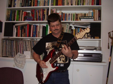 A man, a strat, and a messy book shelf