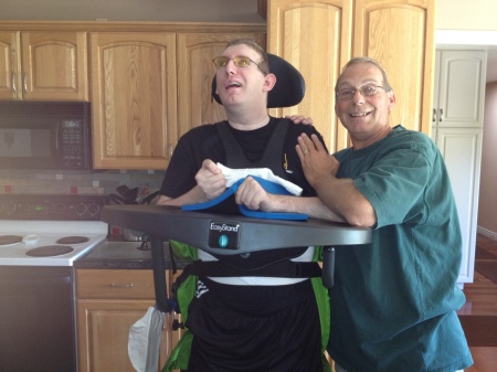 Dave with Evan standing in kitchen with help of his sit to stand  9/2012